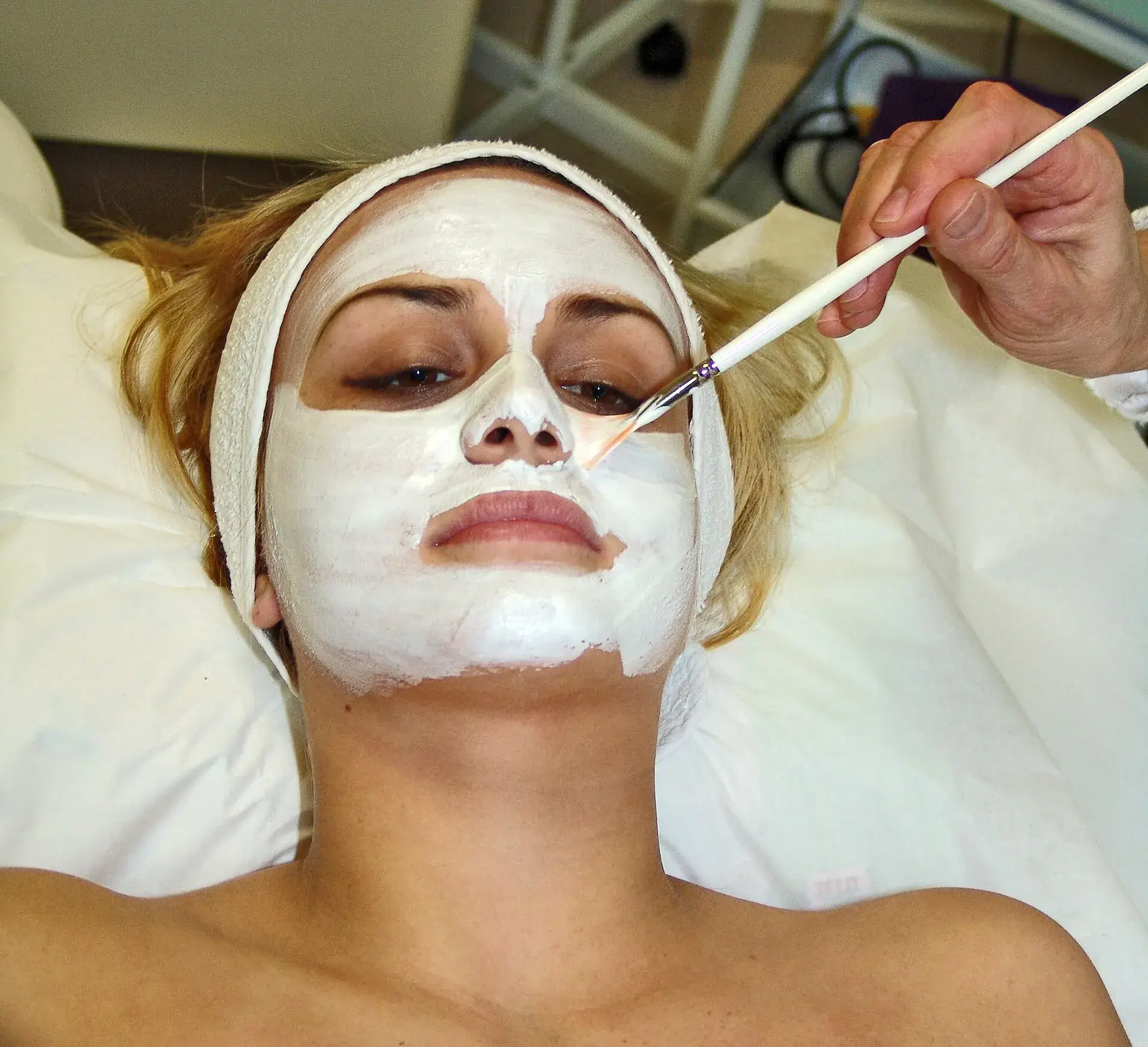 Esteticista profesional aplicando una mascarilla facial a una clienta en el salón